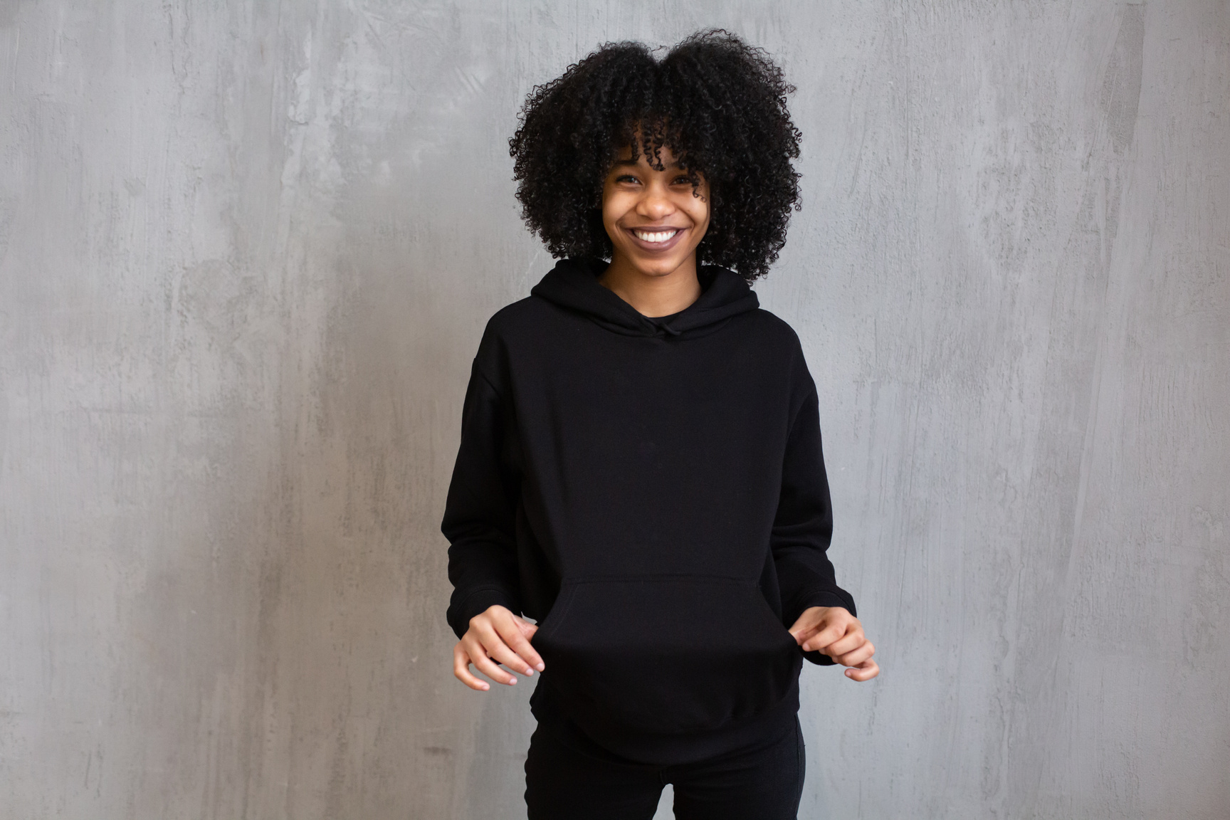 Happy black woman in hoodie standing against shabby gray wall